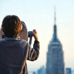 A child uses binoculars to view the Empire State Building in New York City at sunset.
